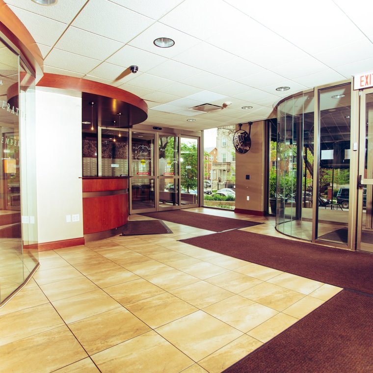 Lobby with glass walls and doors, with light brown tiled floor and darker brown mats