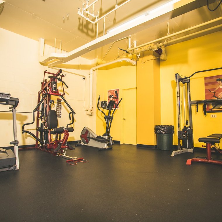 Workout area with treadmill, eliptical, two work out gyms against yellow walls on a black floor