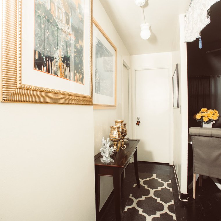 Apartment entrance hallway with dark side wall table against white walls on a black floor and grey and white accent rug